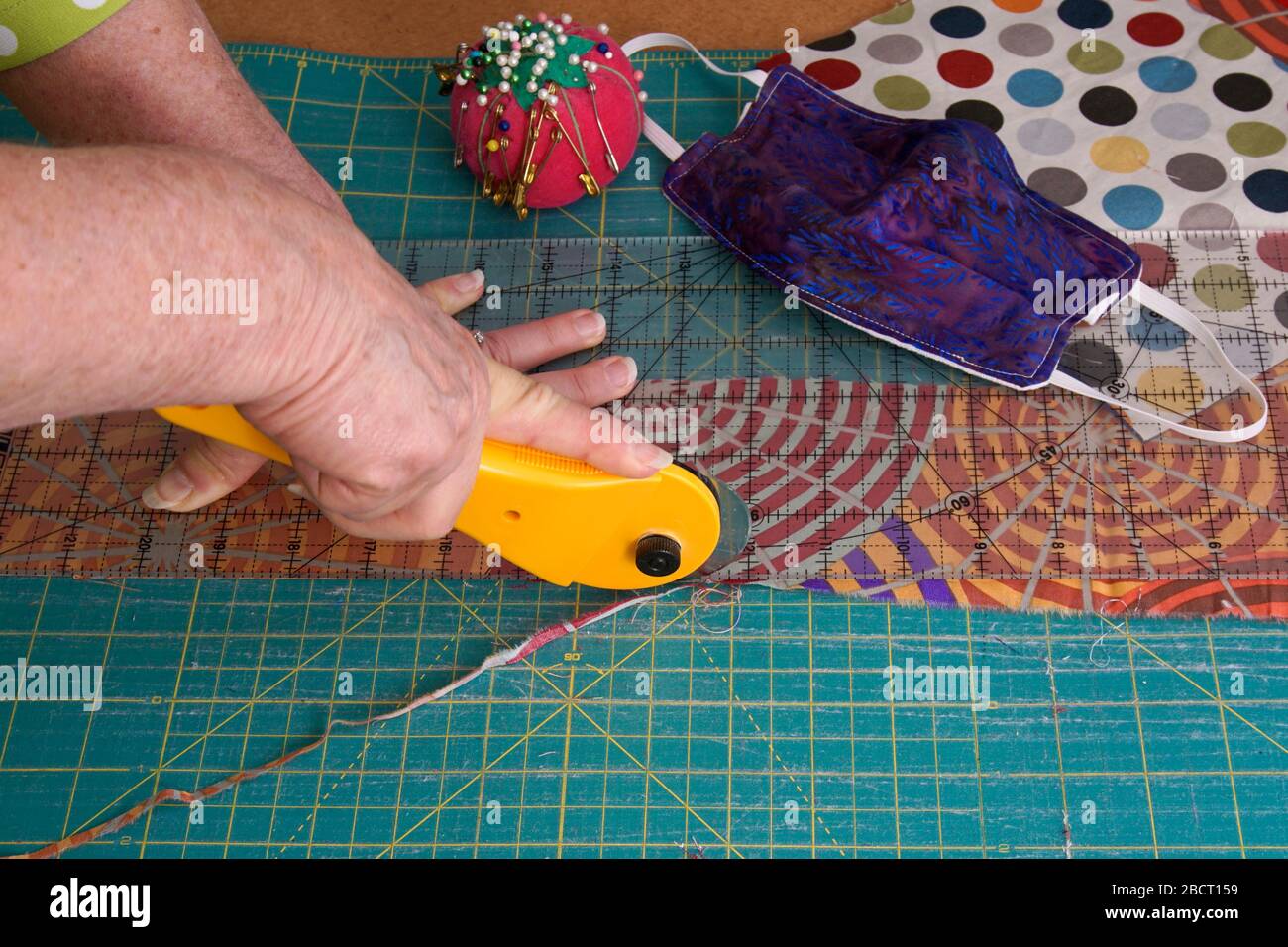 Usando un cortador giratorio para cortar tela acolchada sobrante para máscaras de cara cosidas a mano Foto de stock