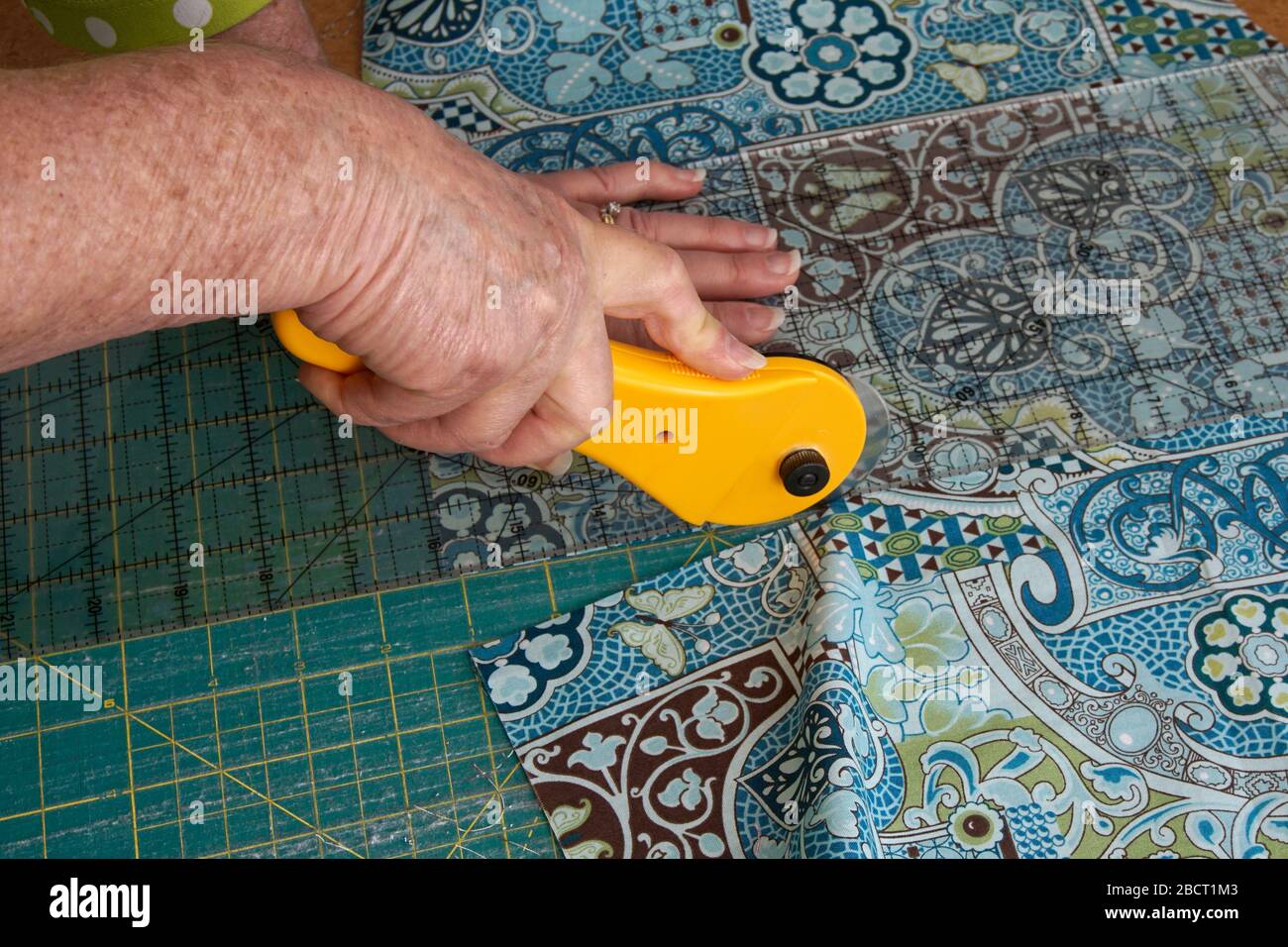 Cierre de las manos de una mujer usando un cortador giratorio para cortar tela acolchada Foto de stock