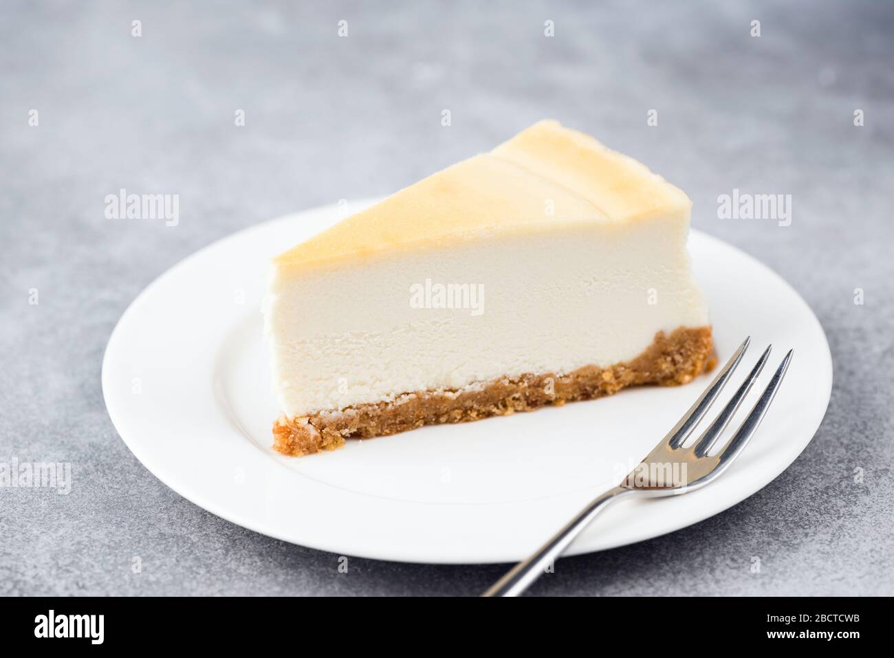 Una rebanada de tarta de queso en un plato blanco. Pastel de postre hecho con queso crema. Aislado sobre fondo de hormigón gris Foto de stock