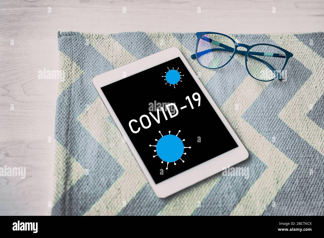 Corona virus noticias en línea leer en casa en la tableta. Vista superior del texto COVID-19 escrito en pantalla táctil negra con dibujo de coronavirus junto a las gafas de lectura. Foto de stock