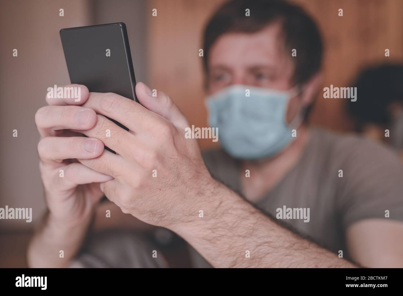 Hombre preocupado usando el teléfono móvil en el hogar cuarentena auto-aislamiento por tener síntomas de Covid-19 coronavirus, enfoque selectivo Foto de stock