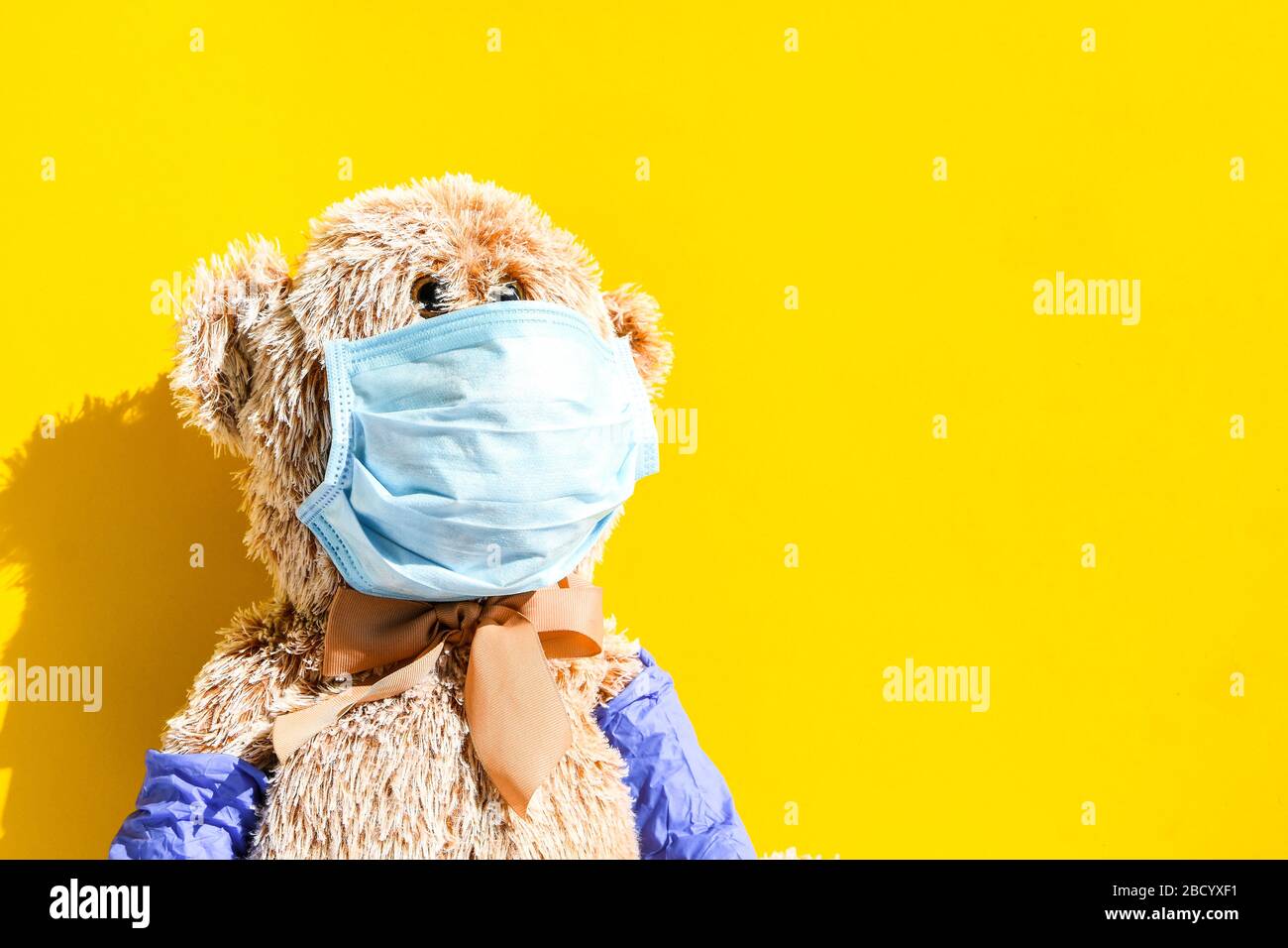 Coronavirus covid-19 y concepto de protección contra la contaminación. Muñeca de oso de peluche con máscara y guantes protectores sobre fondo amarillo, espacio de copia Foto de stock