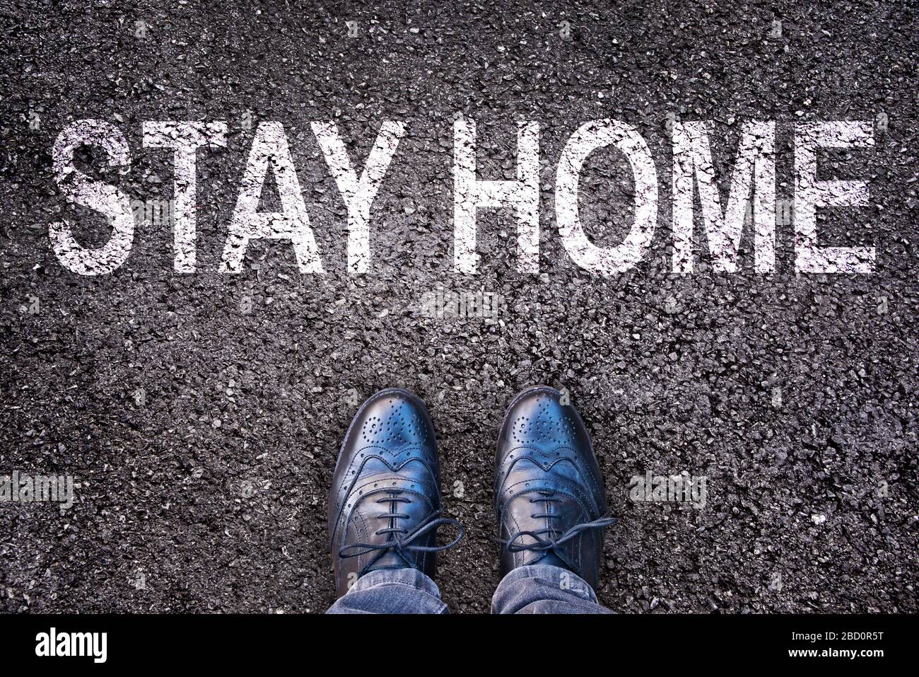 Mensaje manténgase en casa escrito en la calle asfaltada con piernas y zapatos Foto de stock