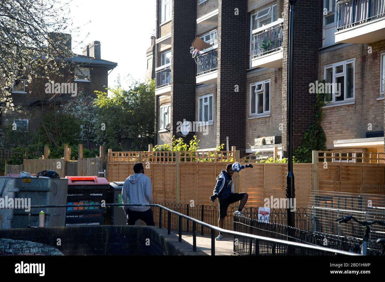 Londres, Hackney. Pandemia de coronavirus. Dos jóvenes juegan al fútbol junto a los bins. Foto de stock