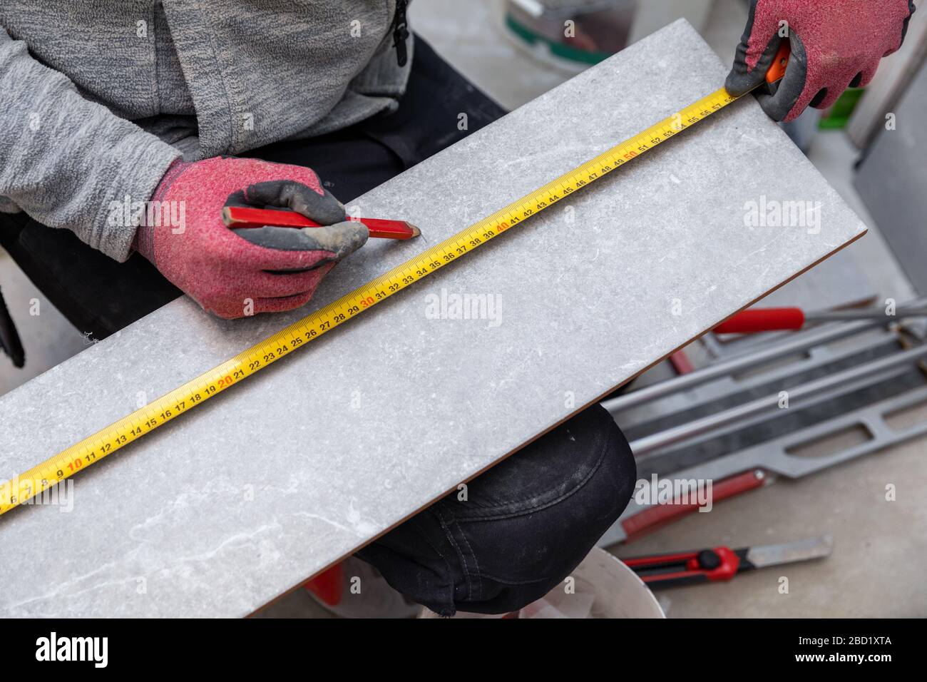 trabajador marcando baldosas de cerámica con lápiz y cinta métrica para cortar Foto de stock