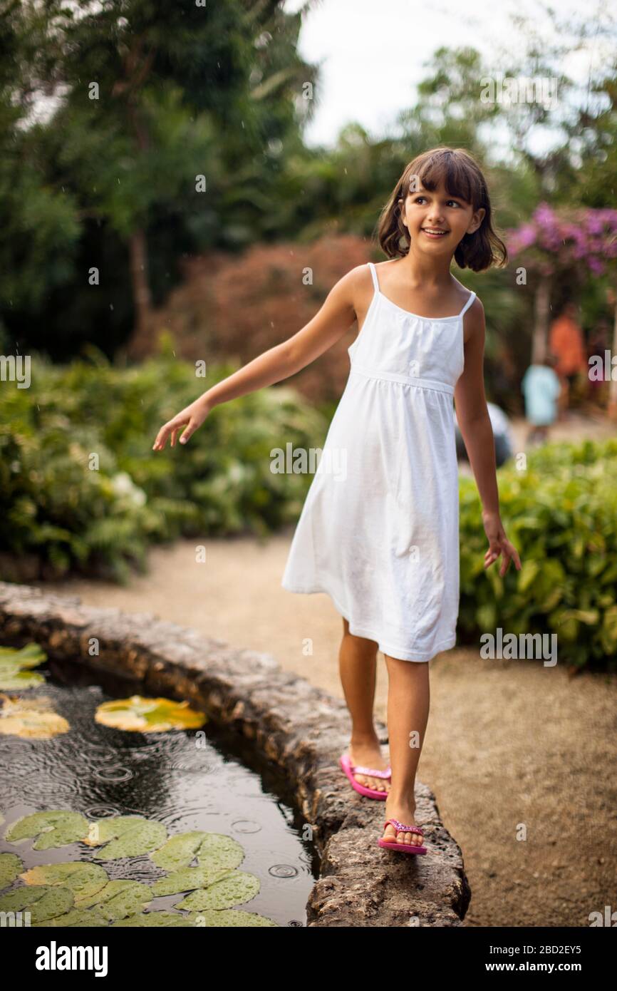 Sonriente joven divirtiéndose equilibrio sobre el muro de piedra de un estanque de jardín. Foto de stock