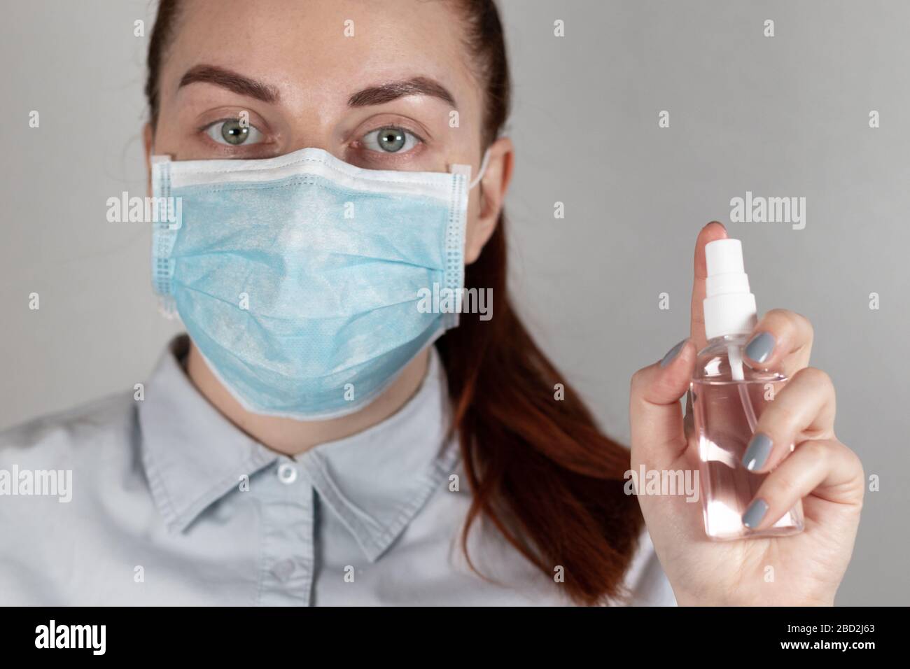Una niña joven doctor en una máscara sostiene un spray desinfectante en su mano sobre un fondo gris. Cierre la persona con un spray limpiador Foto de stock