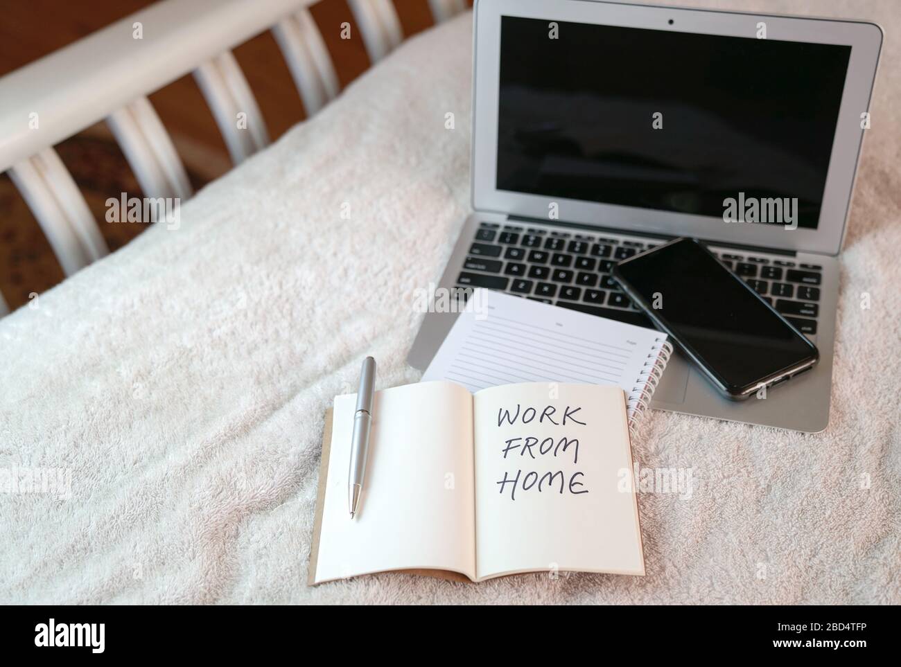 Espacio de trabajo en casa con ordenador portátil y bloc de notas en la parte superior de la cama. Texto, trabajo desde casa escrito en el bloc de notas. Foto de stock