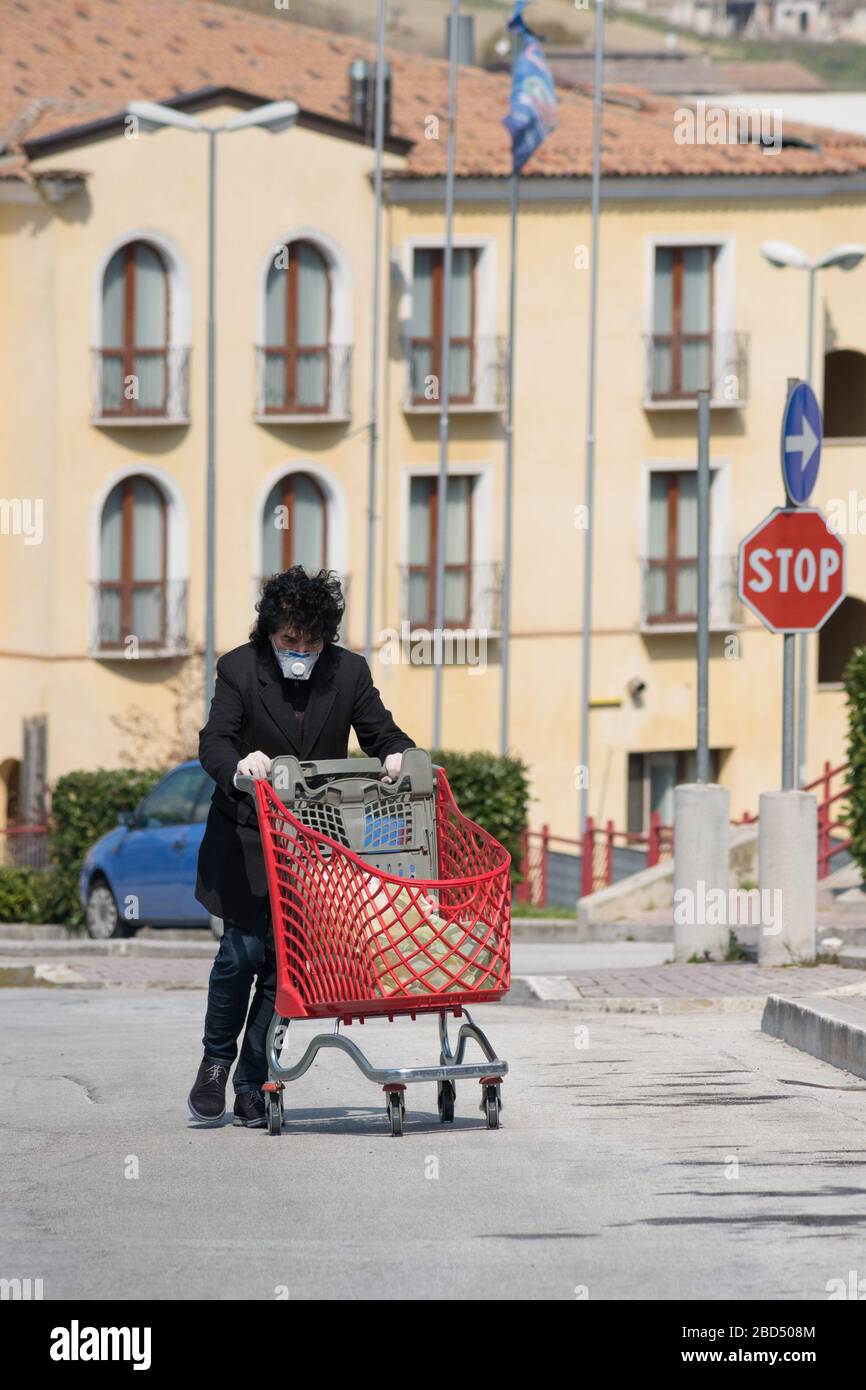 Campobasso,Molise Region,Italia:un hombre con guantes y máscara protectora regresa a casa y empuja un carro de compras hecho en un supermercado en Campobasso (Ital Foto de stock
