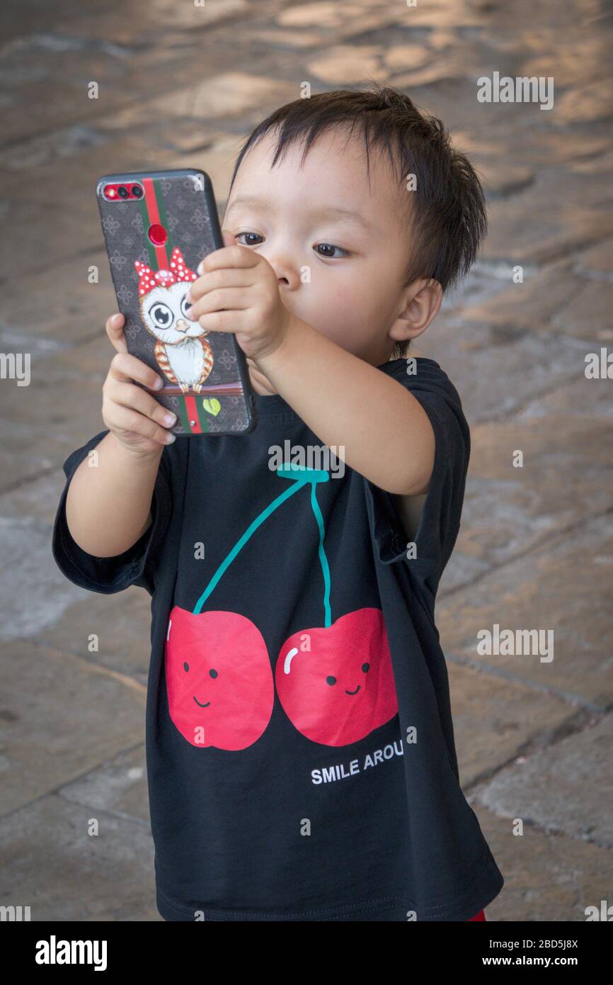 Niño chino jugando con el gran teléfono móvil de sus padres, China Foto de stock