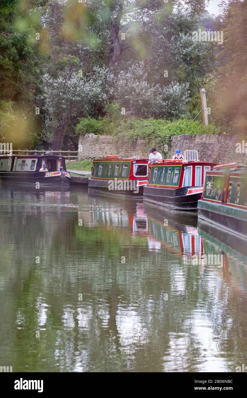 Barcos estrechos en el canal Kennet y Avon en Bradford-on-Avon, Wiltshire, Reino Unido con alguien pescando el canal Foto de stock