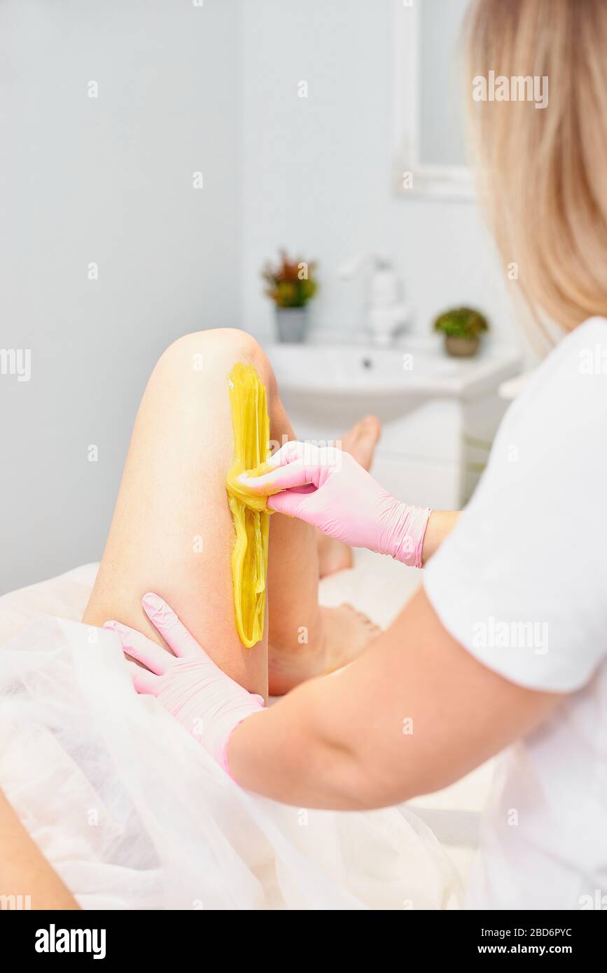 Concepto de depilación y belleza -Beautician depilando piernas de mujeres  jóvenes con azúcar líquido en el centro de spa. Depilación de piernas con  pasta amarilla de rugido Fotografía de stock - Alamy