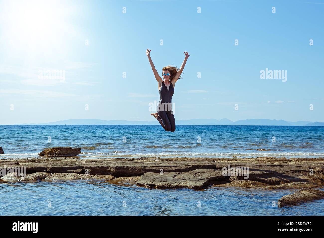 Mujer atlética alegremente salta en lo alto de la playa Foto de stock