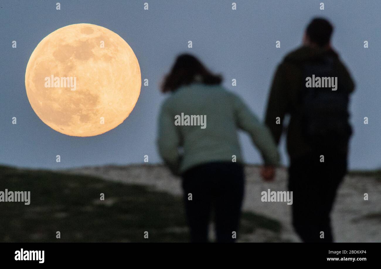 Hanover, Alemania. 07 de abril de 2020. Una pareja está caminando mano-sostenido hasta Kronsberg cuando la luna se levanta en el horizonte como la llamada superluna. La luna alcanza su perigeo, es decir, el punto más cercano a la órbita de la Tierra, en la noche del 7-8 de abril como luna llena y por lo tanto parece particularmente grande para el observador humano. Crédito: Julian Stratenschulte/dpa/Alamy Live News Foto de stock