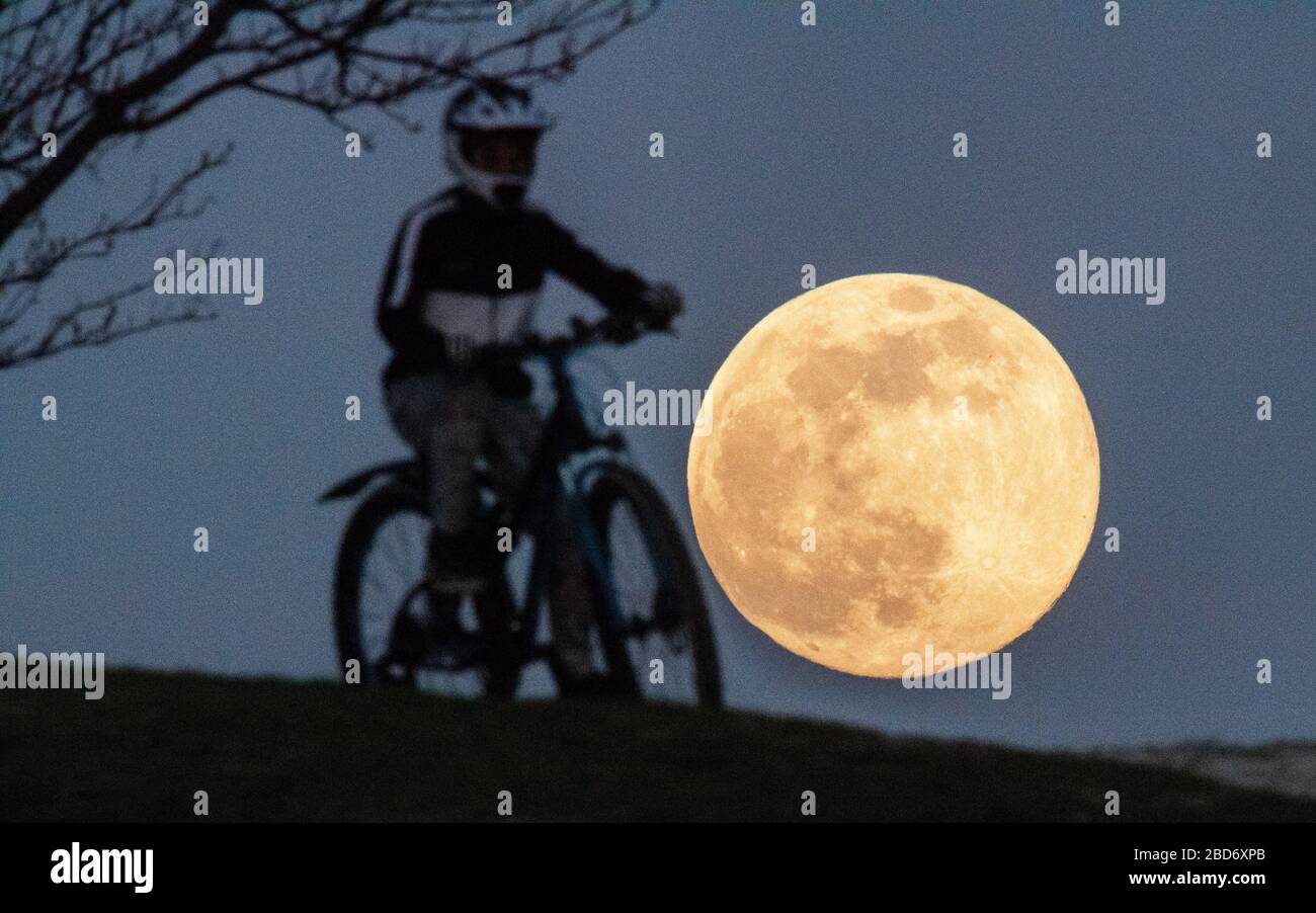 Hanover, Alemania. 07 de abril de 2020. Un niño en bicicleta está subiendo Kronsberg cuando la luna se eleva en el horizonte como la llamada supermendra. La luna alcanza su perigeo, es decir, el punto más cercano a la órbita de la Tierra, en la noche del 7-8 de abril como luna llena y por lo tanto parece particularmente grande para el observador humano. Crédito: Julian Stratenschulte/dpa/Alamy Live News Foto de stock