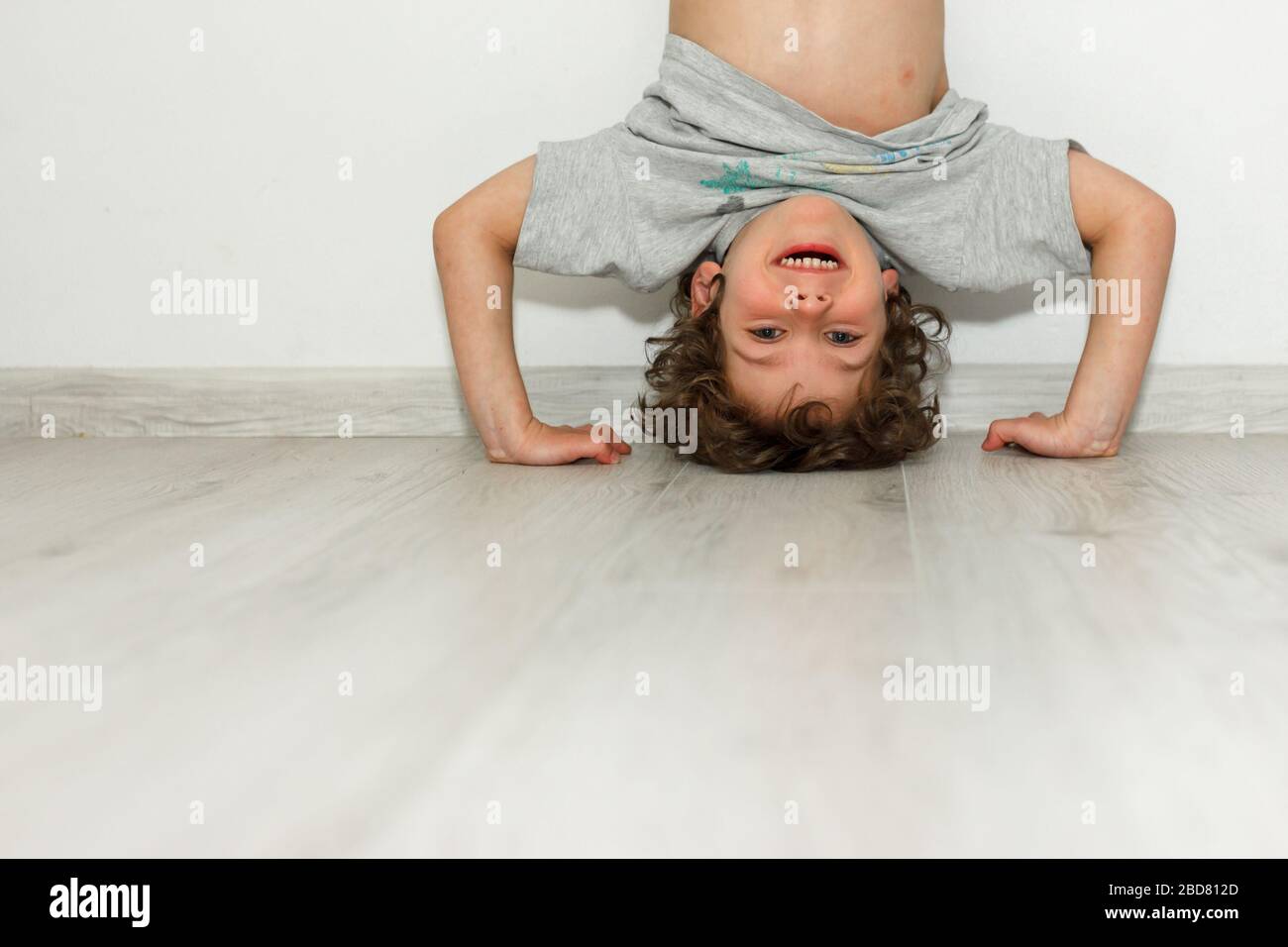 Pequeño niño lindo sonriente que se divierte de pie con las manos al revés cabeza abajo sentir emoción positiva riendo divertido bebé niño regocijándose en la pared blanca Foto de stock