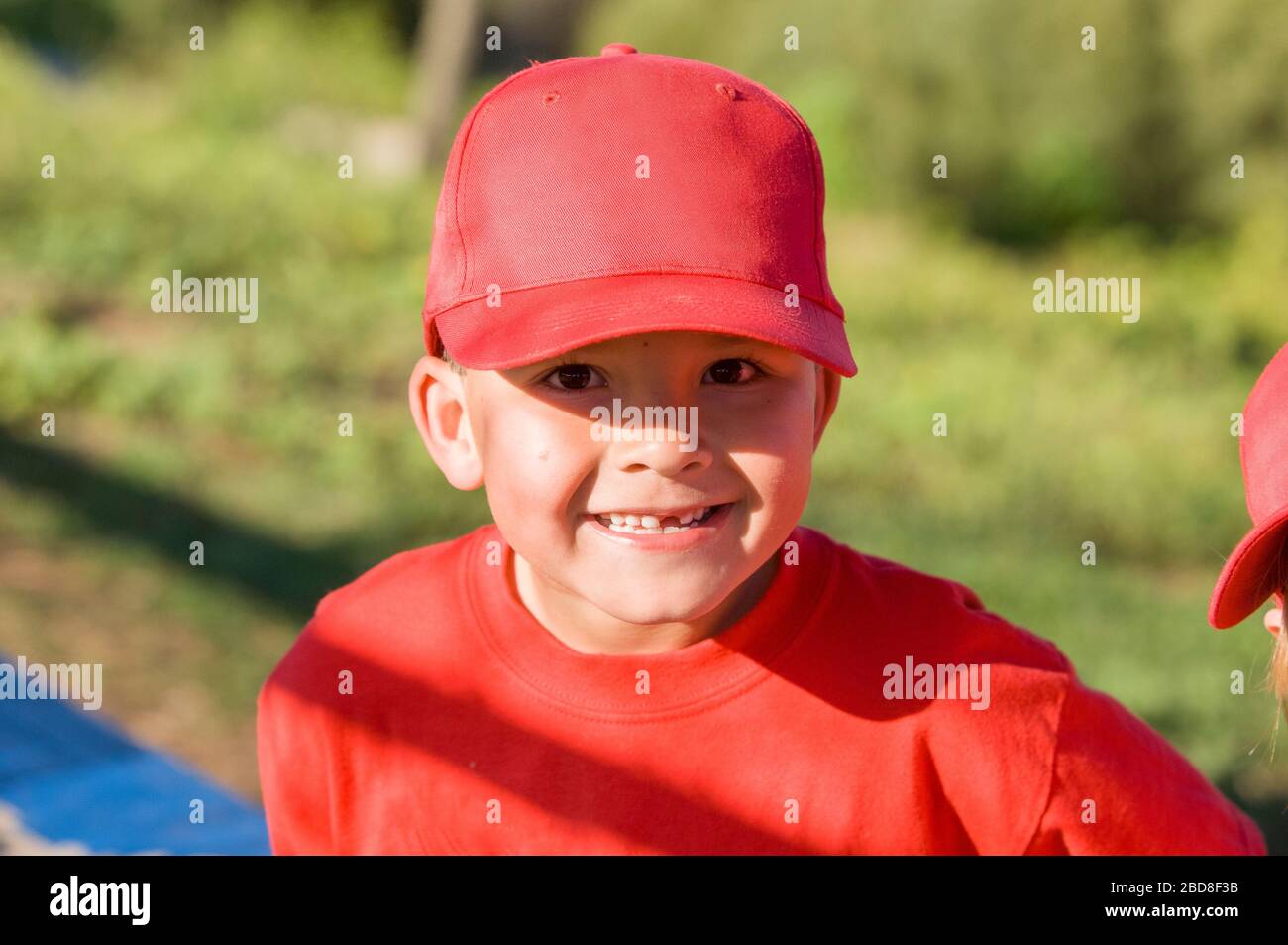 Un niño pequeño que falta un diente en la gorra roja de béisbol sonriendo a la cámara Foto de stock