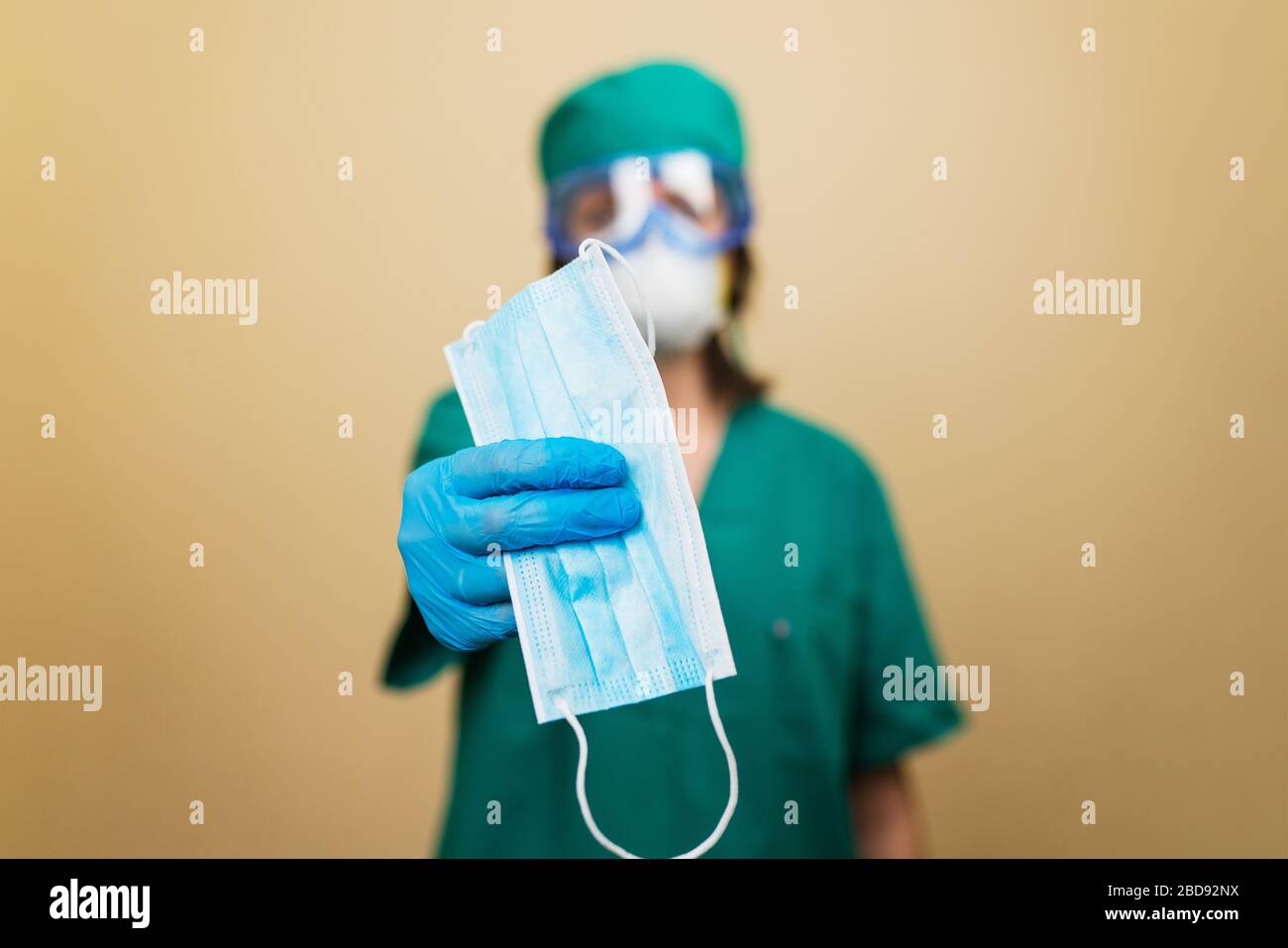 Mujer doctor en traje verde sostiene máscara médica en el had con guante azul en el fondo amarillo. Concepto médico. Enfoque selectivo. Foto de stock
