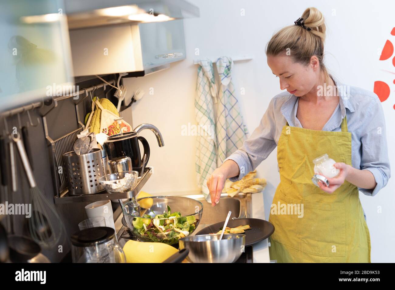 Estancia en casa ama de casa mujer cocinar en la cocina, salando el plato en una cacerola, preparando la comida para la cena familiar. Foto de stock
