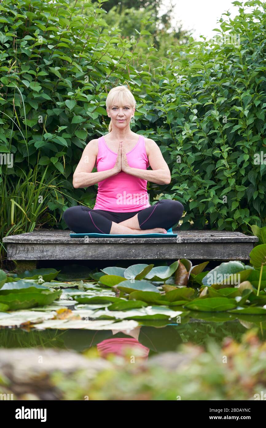 Retrato de la mujer madura en posición de yoga en el embarcadero de madera meditando en el lago Foto de stock