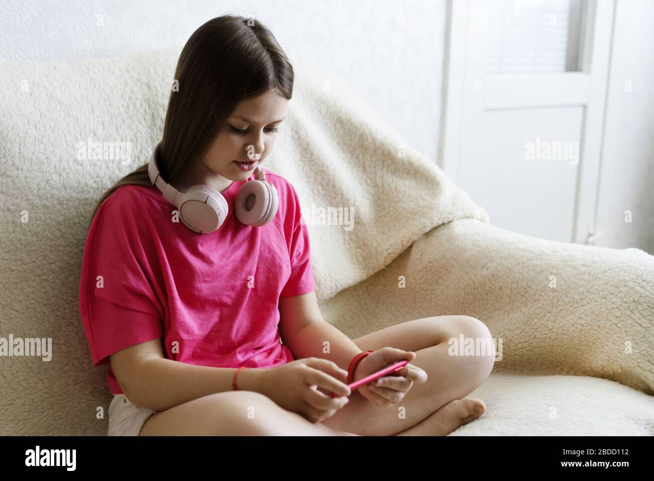 Alegre chica con auriculares de color rosa se sienta con un teléfono en la mano Foto de stock