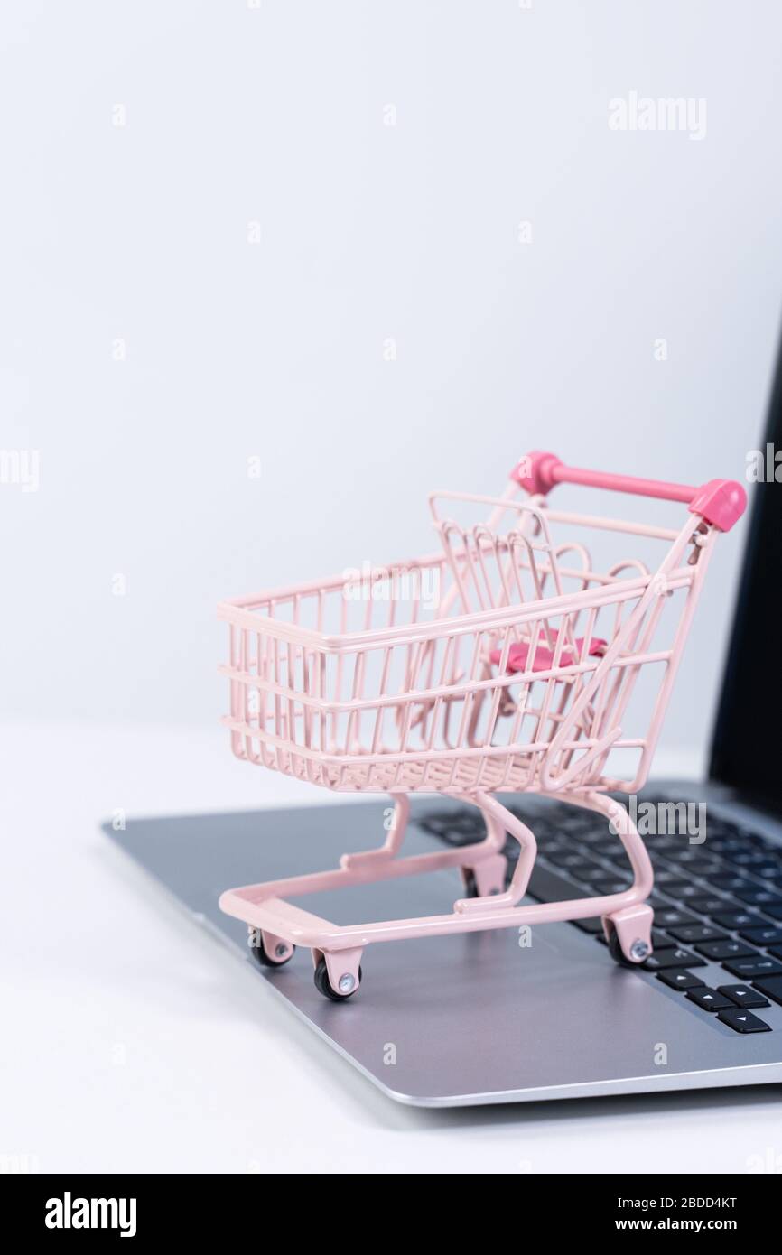 Compras en línea. Mini carro de compras rosa vacío sobre un ordenador portátil sobre fondo de mesa blanco, comprar en casa concepto, primer plano Fotografía de stock -
