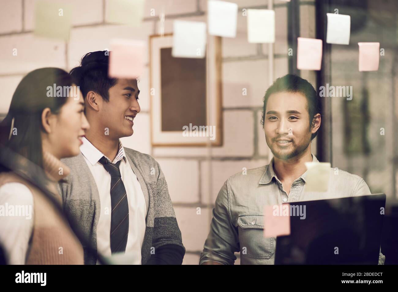 tres pequeños empresarios asiáticos empresarios jóvenes empresarios que se entretienen discutiendo en la oficina utilizando notas pegajosas Foto de stock
