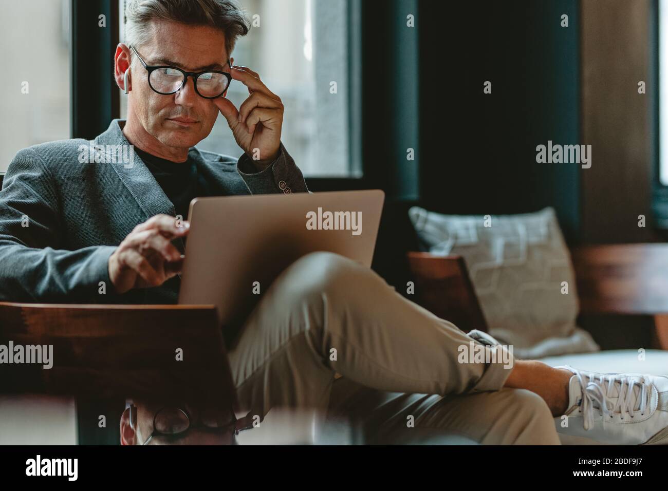 Profesional corporativo de negocios sentado en el vestíbulo de la oficina trabajando con un ordenador portátil. Un ejecutivo masculino maduro que trabaja en un salón de oficinas. Foto de stock
