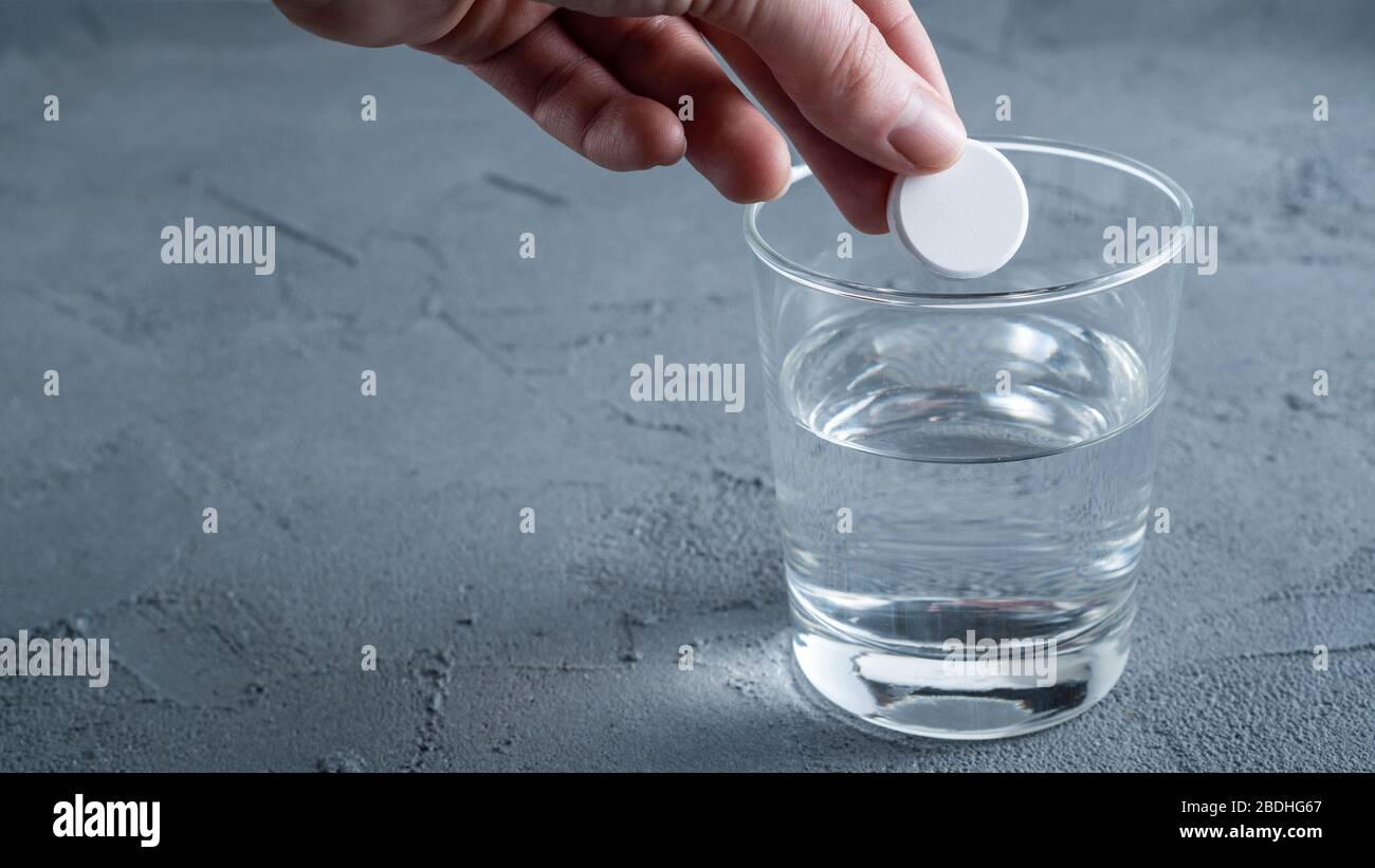 Una tableta de aspirina efervescente se lanza en un vaso de agua. Fondo con espacio para texto. Foto de stock