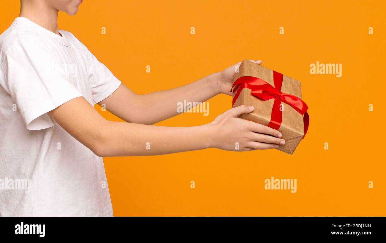 Caja de regalo en manos de niño adolescente, fondo naranja Foto de stock