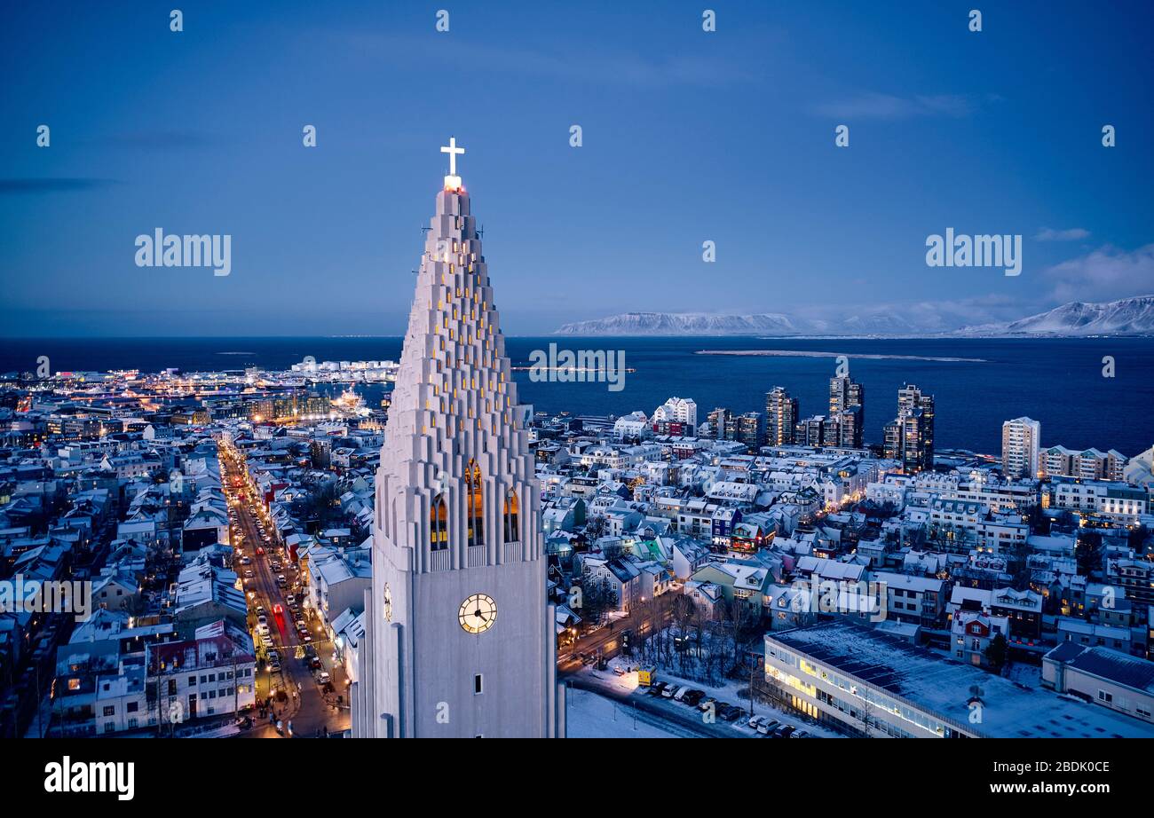 Vista aérea de la moderna torre blanca de la alta iglesia Hallgrimskirkja con una cruz brillante en el centro moderno de la ciudad al atardecer en Islandia Foto de stock