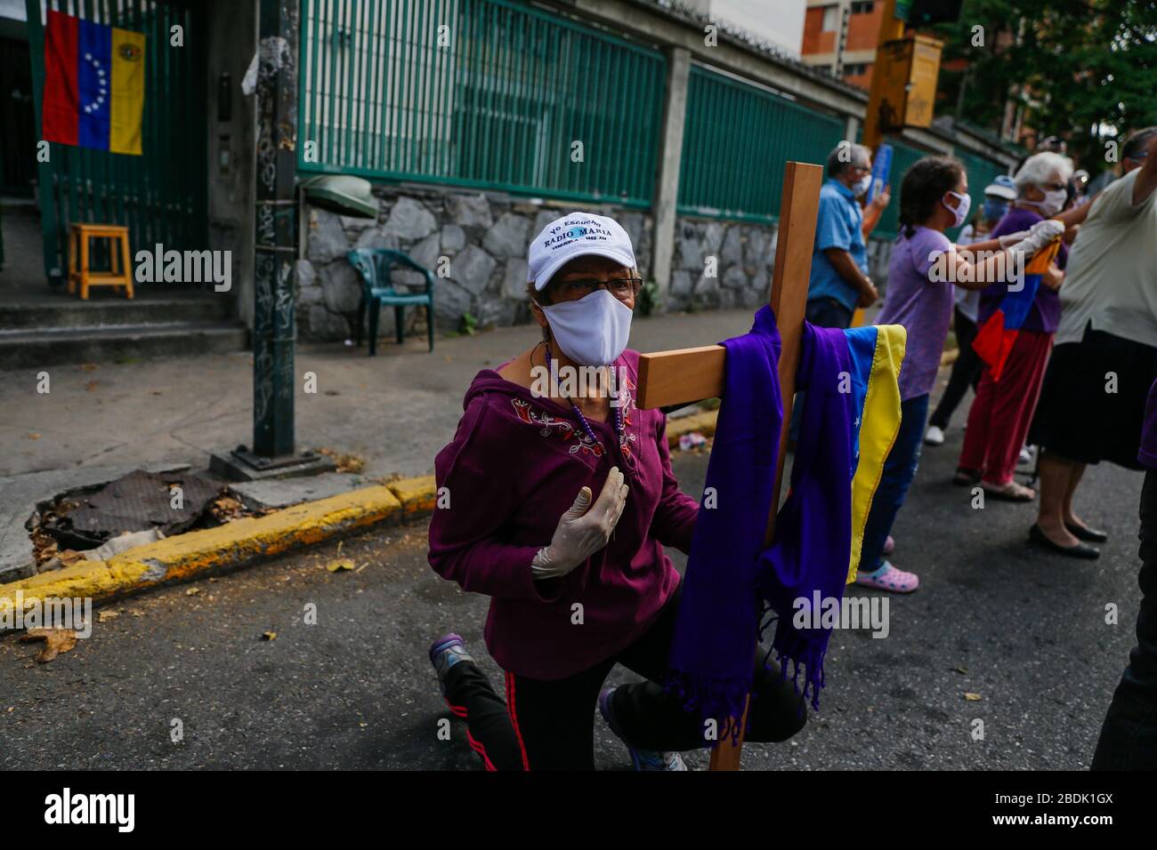 Caracas, Venezuela. 08 de abril de 2020. Una mujer con máscara facial y  guantes de látex se arrodilla junto a una cruz, ya que la figura de Jesús  'Nazareno de San Pablo'