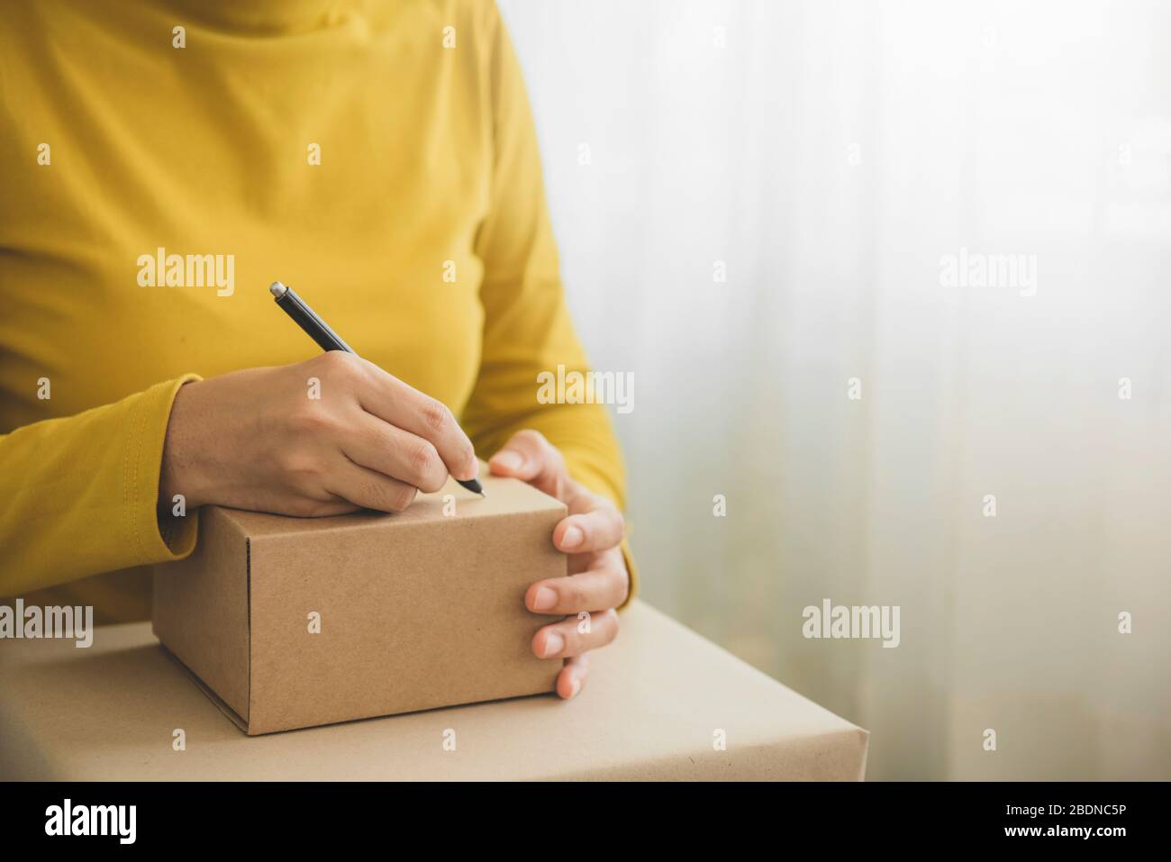Mujer joven trabajando y escribiendo la dirección del cliente en la caja  del paquete del embalaje para enviar el pedido al cliente en la oficina de  casa, compras en línea, la pequeña