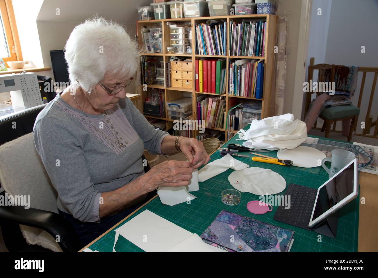 Mujer anciana que hace sombreros de equipo de protección personal (PPE) para NHS en la crisis de Covid-19 Foto de stock