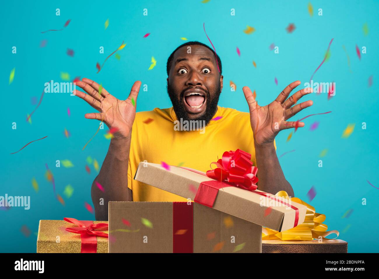 Feliz y asombrado hombre abre regalos en su cumpleaños. Aislado sobre fondo cian Foto de stock