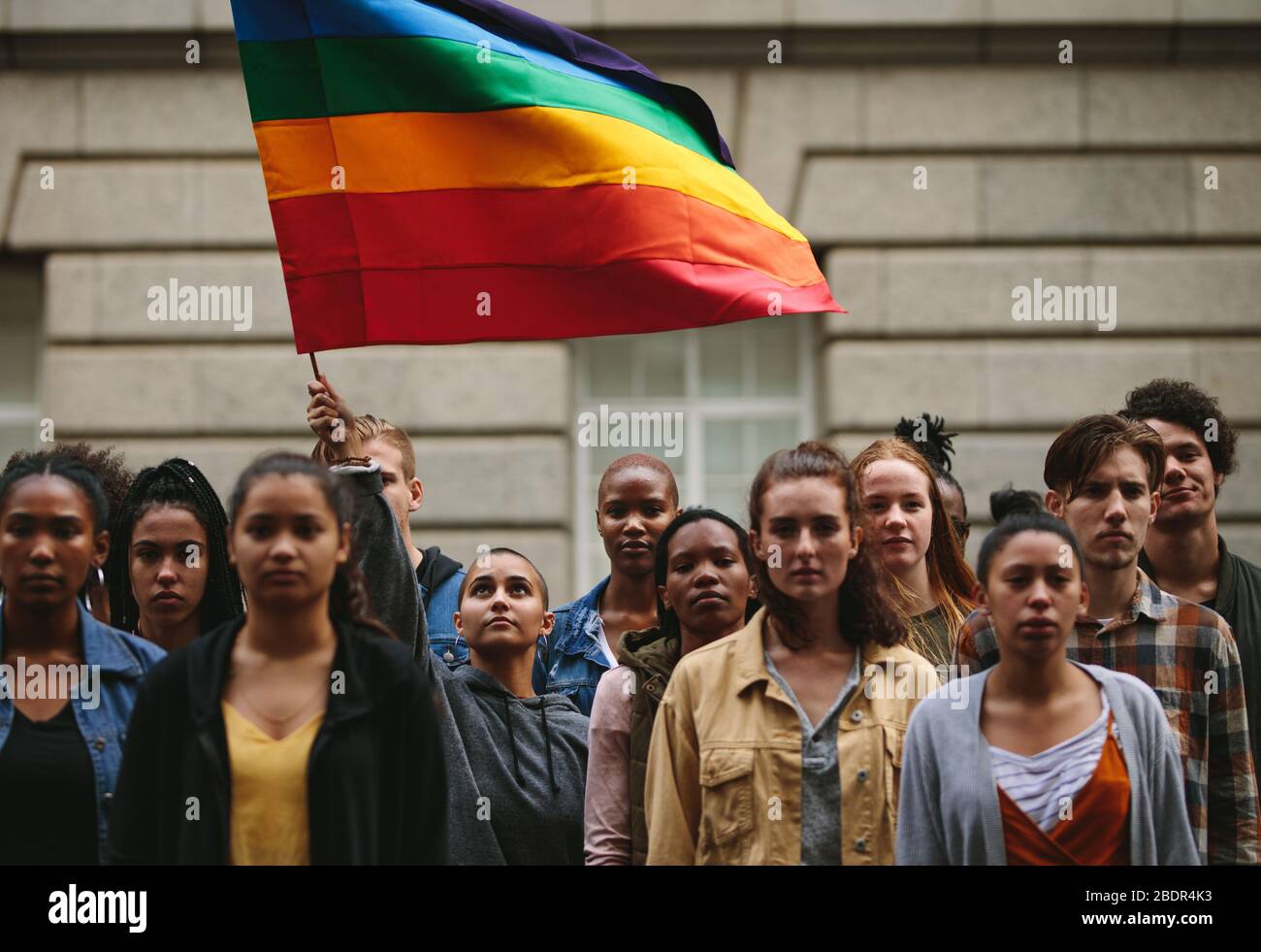 La gente participa en el desfile de orgullo. Gente multiétnica en la calle de la ciudad con una mujer que ondea la bandera del arco iris gay. Foto de stock