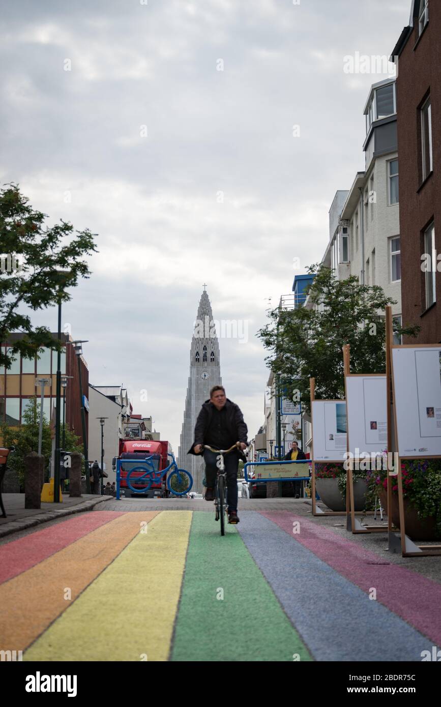 Un hombre paseando en bicicleta por una calle arco iris en Reykjavik con el icónico Hallgrímskirkja detrás, Islandia Foto de stock