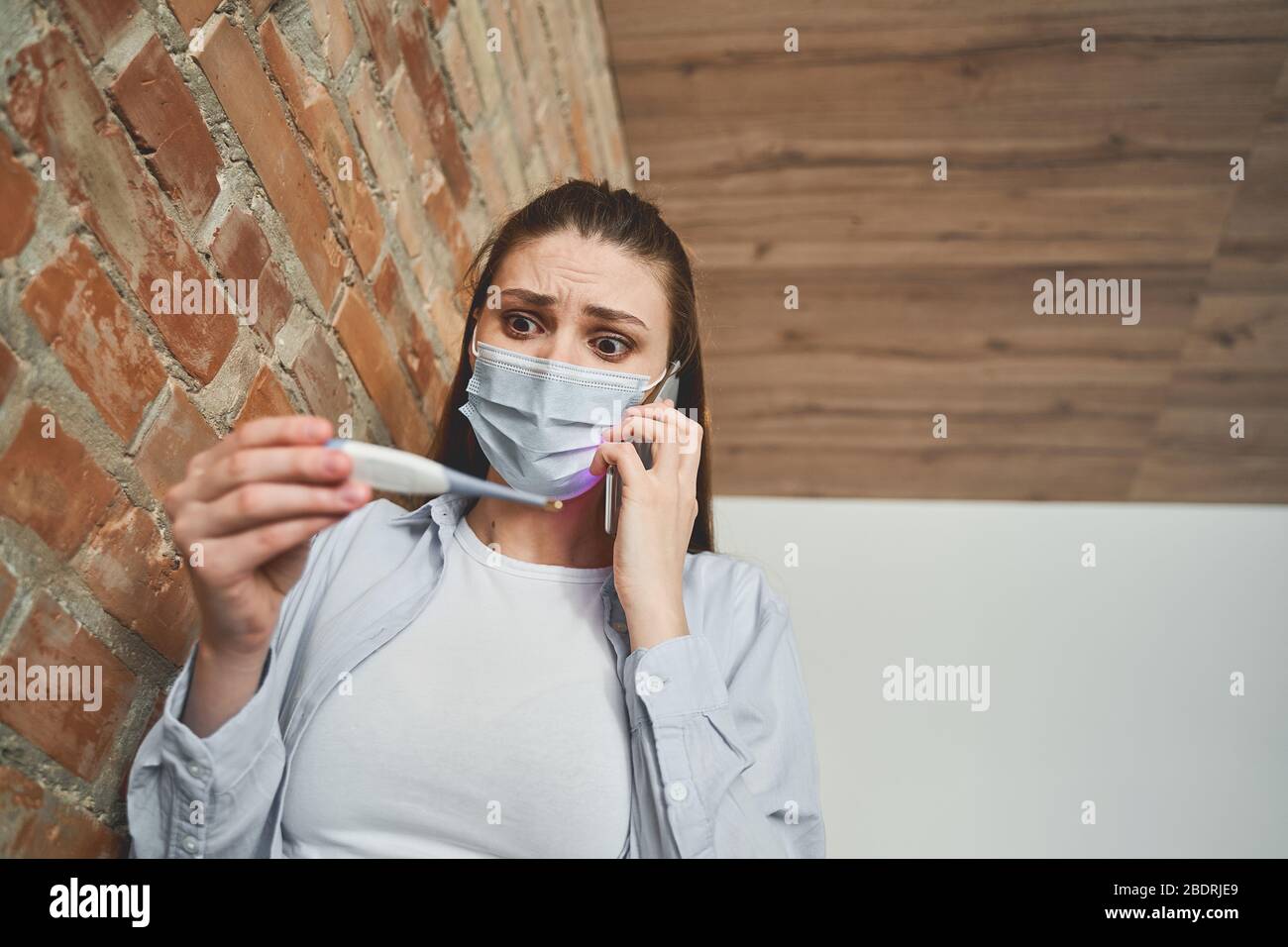 Mujer caucásica joven asustada sosteniendo un termómetro Foto de stock