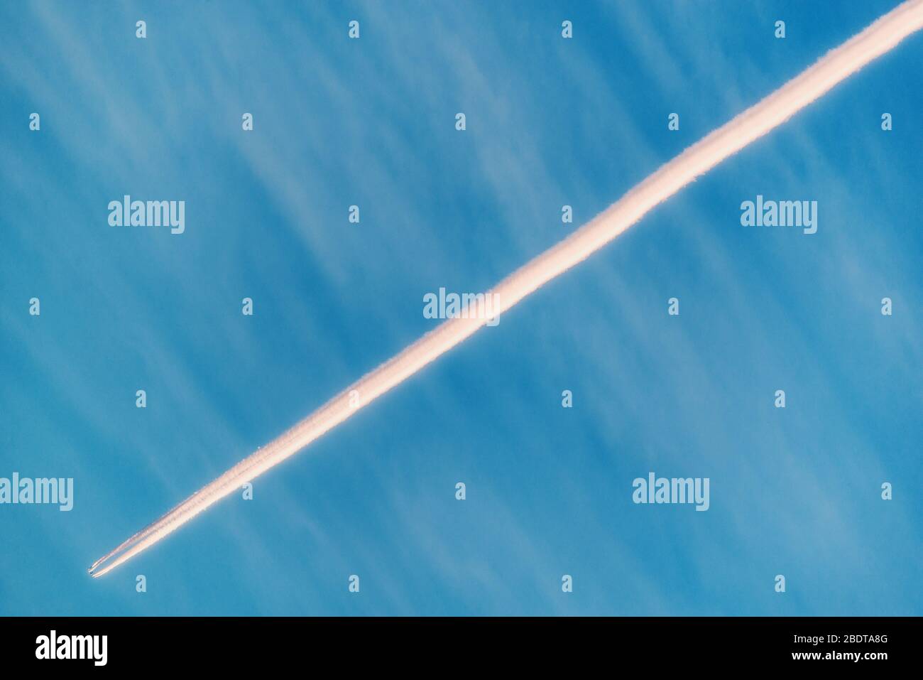 Un largo sendero de avión jet en el cielo azul al atardecer. Foto de stock