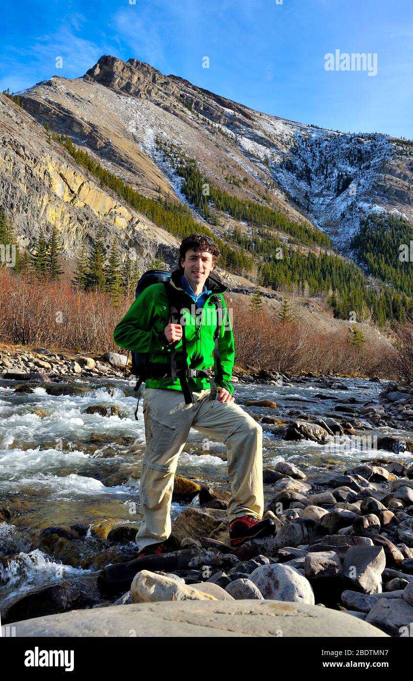 Un hombre solitario vestido con ropa colorida cruzando un rápido arroyo en las montañas rocosas de Alberta, Canadá Foto de stock