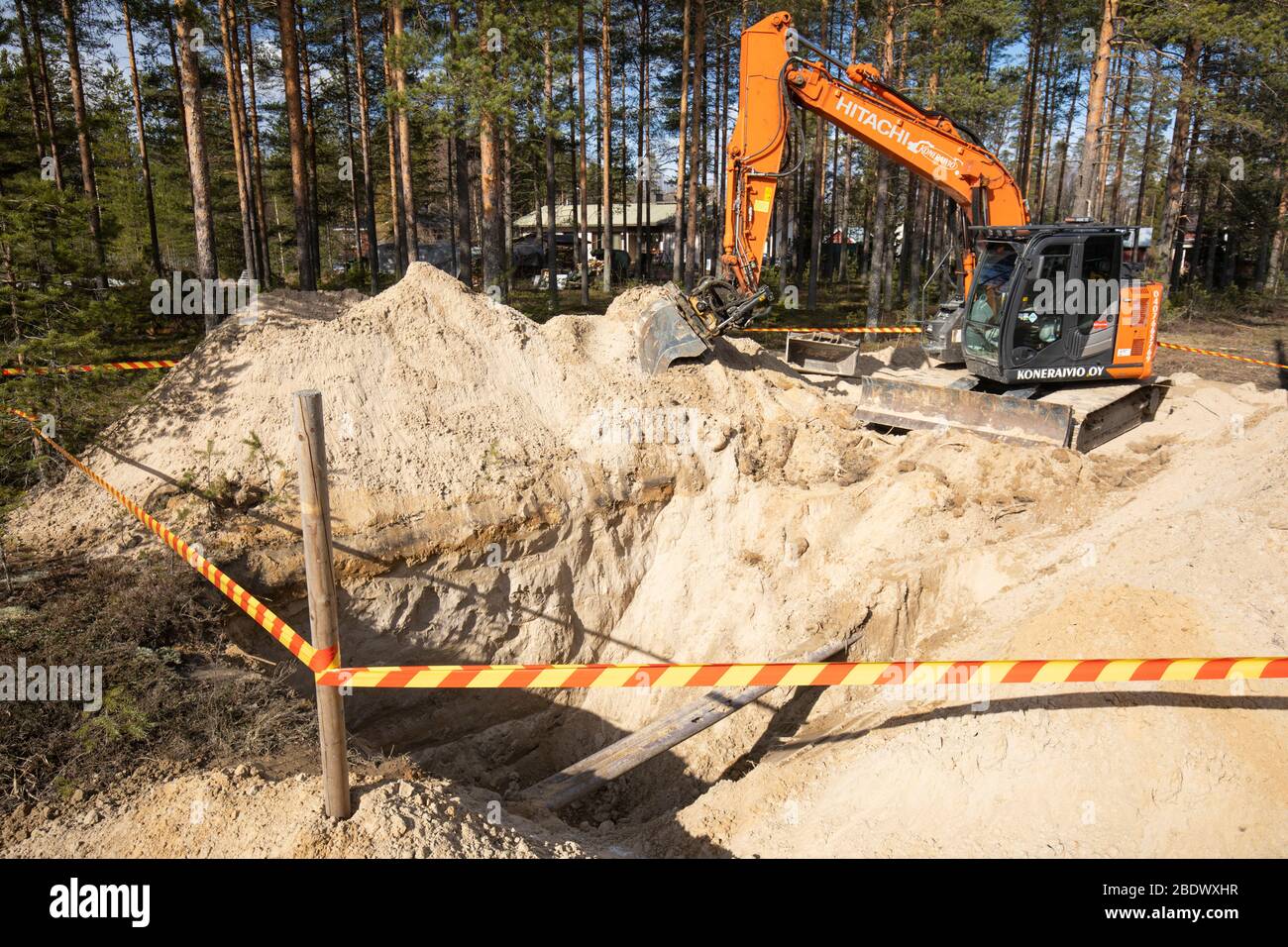 Naranja Hitachi digger y una zanja profunda en suelo arenoso, Finlandia Foto de stock