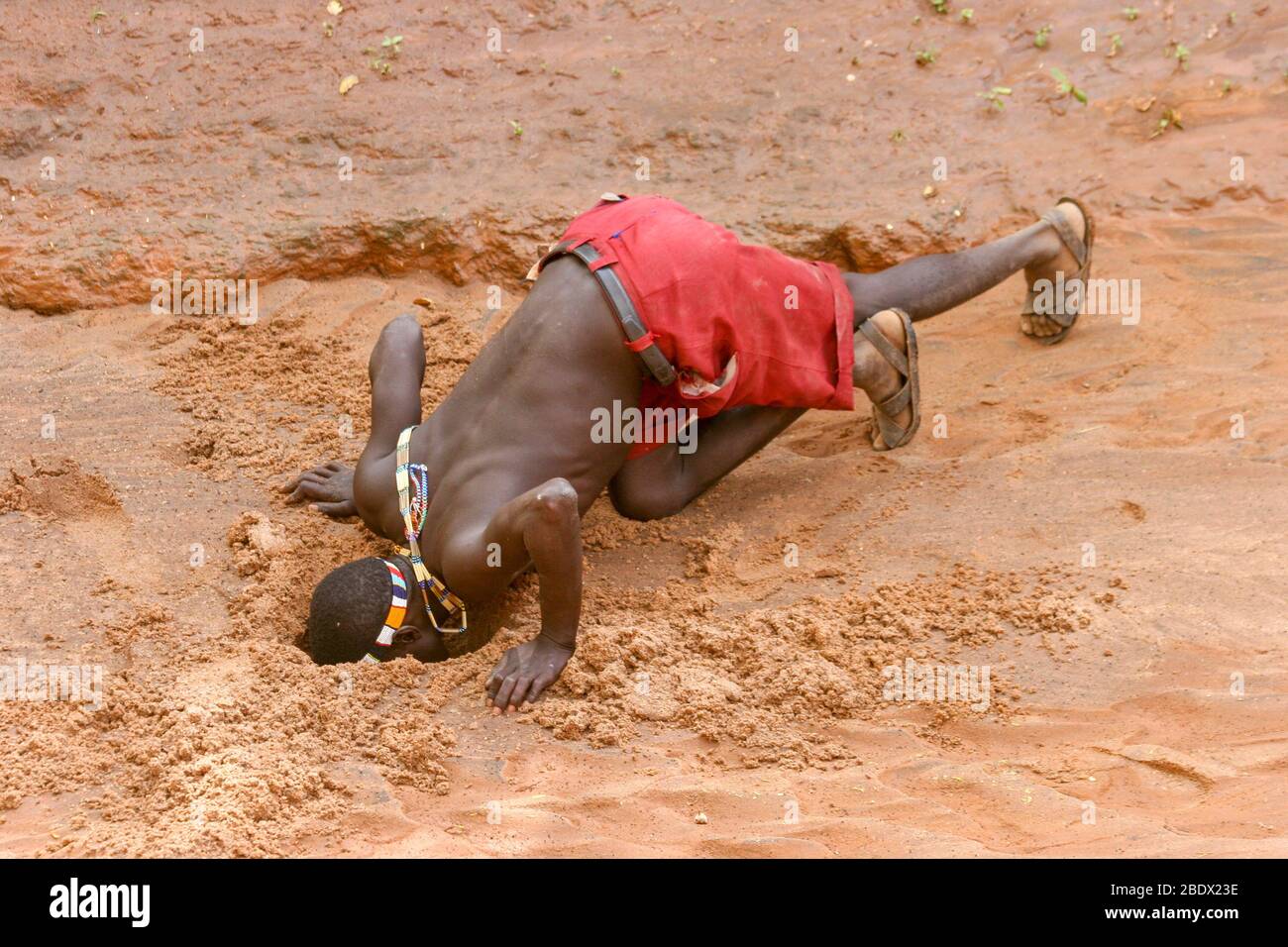 Hombres de Hadza bebiendo agua de un agujero de agua fangoso casi seco. Hadza es una pequeña tribu de cazadores recolectores AKA Hadzabe Tribe. Fotografiado en el lago Eyasi, Foto de stock