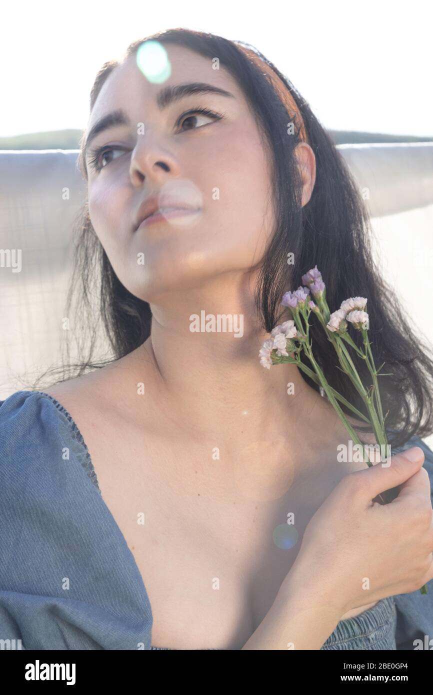 Mujer étnica bonita fuera sosteniendo flores con iluminación única Foto de stock