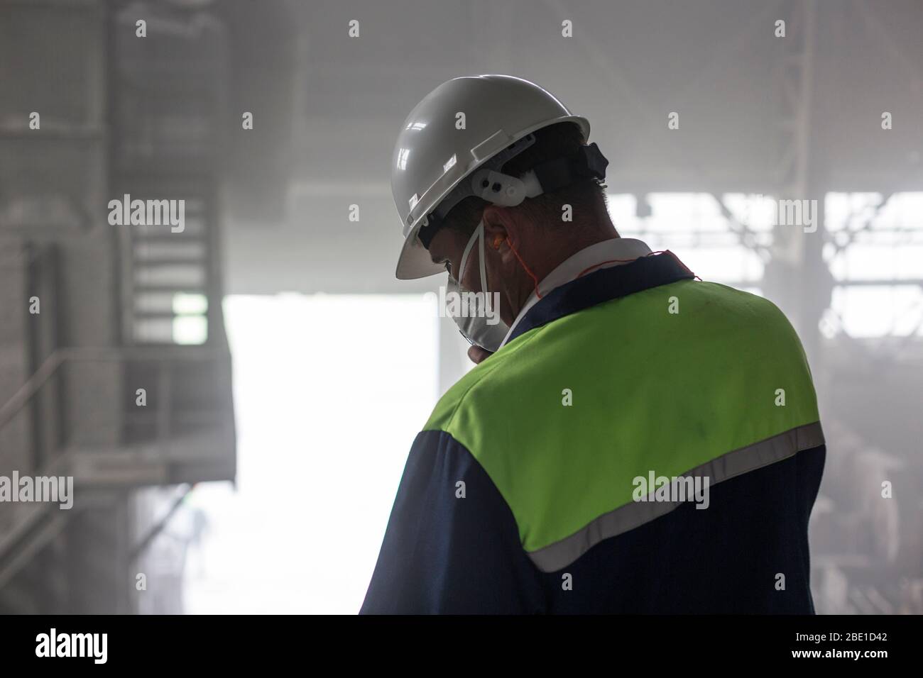 Un ingeniero de minería en casco blanco y respirador inspecciona un taller sucio y polvoriento Foto de stock