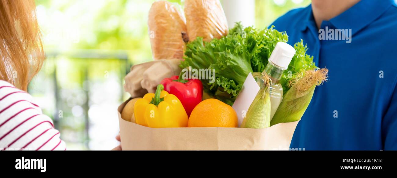 Entrega de tienda de comestibles hombre en uniforme azul entrega de alimentos a una mujer cliente en casa, tamaño de la bandera Foto de stock