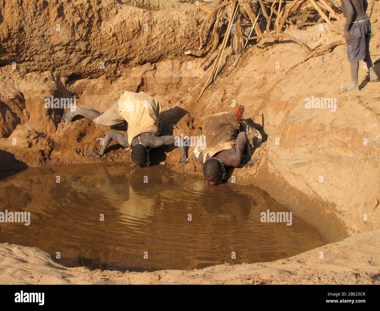 Hombres de Hadza bebiendo agua de un agujero de agua fangoso casi seco. Hadza es una pequeña tribu de cazadores recolectores AKA Hadzabe Tribe. Fotografiado en el lago Eyasi, Foto de stock