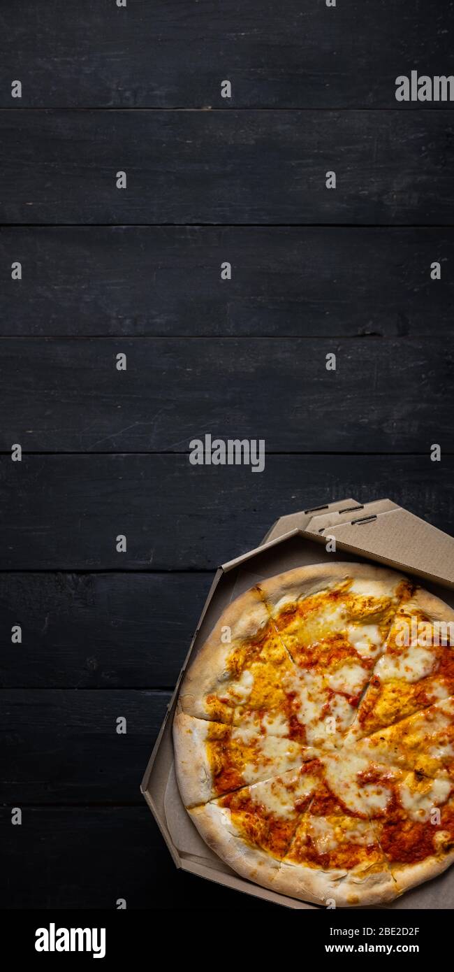 Pizza margherita en una caja abierta, fondo oscuro con espacio de texto.  Comida para llevar, comida para llevar concepto: Pila de cajas de pizza en  la parte posterior de madera negra Fotografía