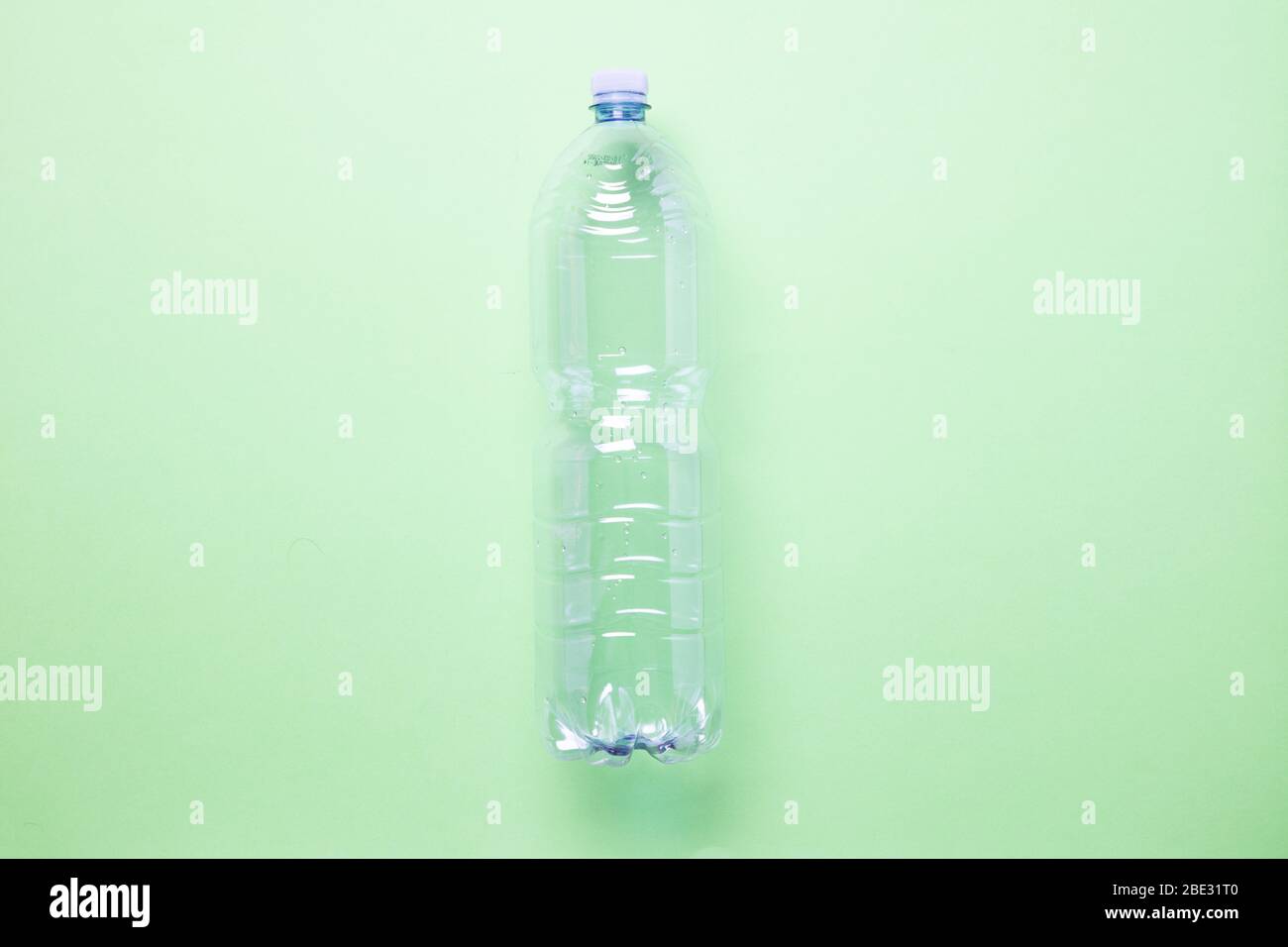 una botella de plástico vacía minimalista, en el centro de la imagen, sobre un fondo verde claro pastel, una capa plana, un estudio de disparo Foto de stock