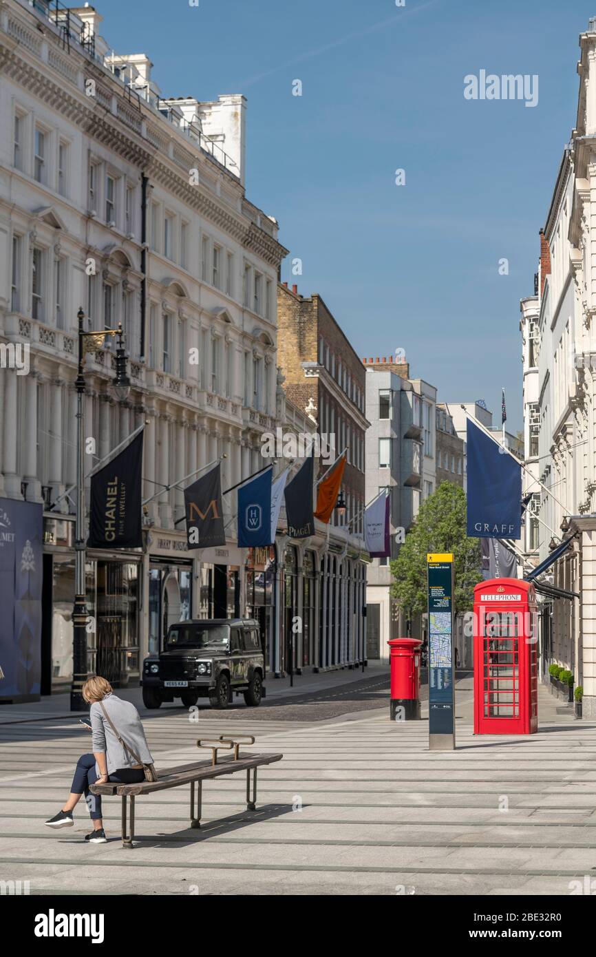 Una mujer sentada sola en una calle comercial vacía y tranquila de Londres durante la pandemia de Coronavirus covid 19, impuso el bloqueo. Las tiendas están cerradas. Foto de stock