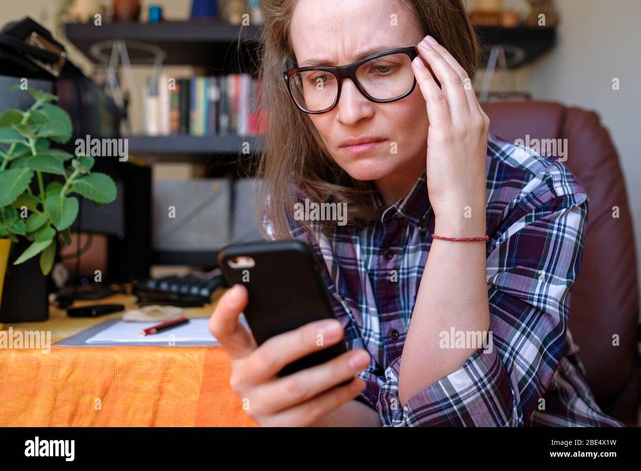 Una mujer lee noticias de un teléfono móvil. Sostiene su cabeza, gambas. Malas emociones. Foto de stock